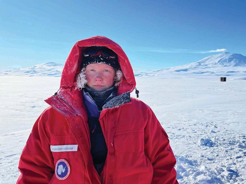 Marissa Tremblay在南极洲报道. 她穿着一件大红色大衣，戴着兜帽.